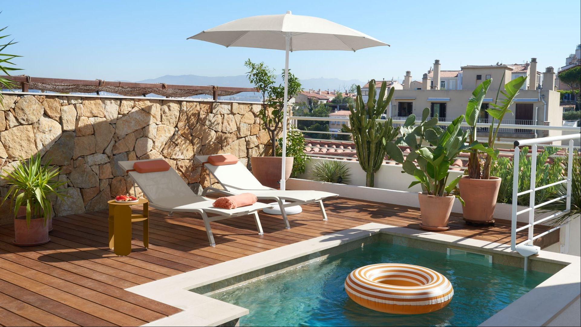 Terraza con piscina con sombrilla blanca, tumbonas blancas, suelo de madera, plantas